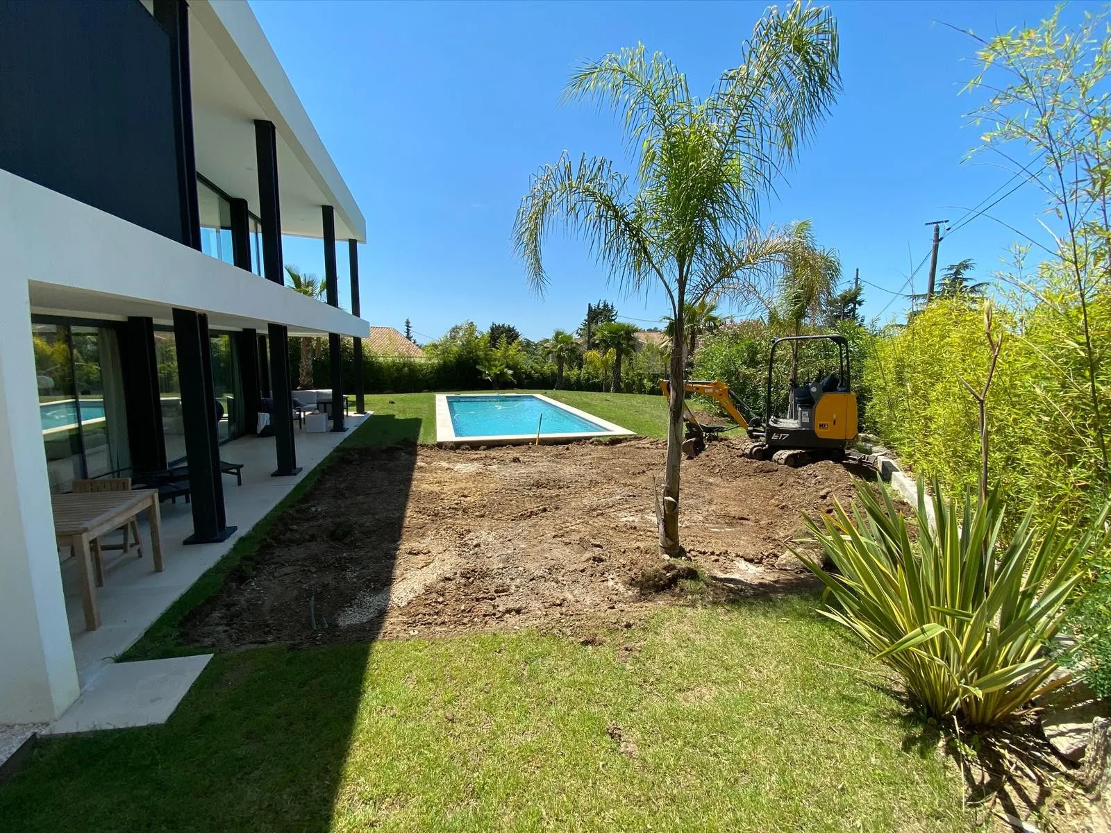 La même villa en chantier, pelouse arrachée autour du bassin, mini-pelle en place — avant aménagement