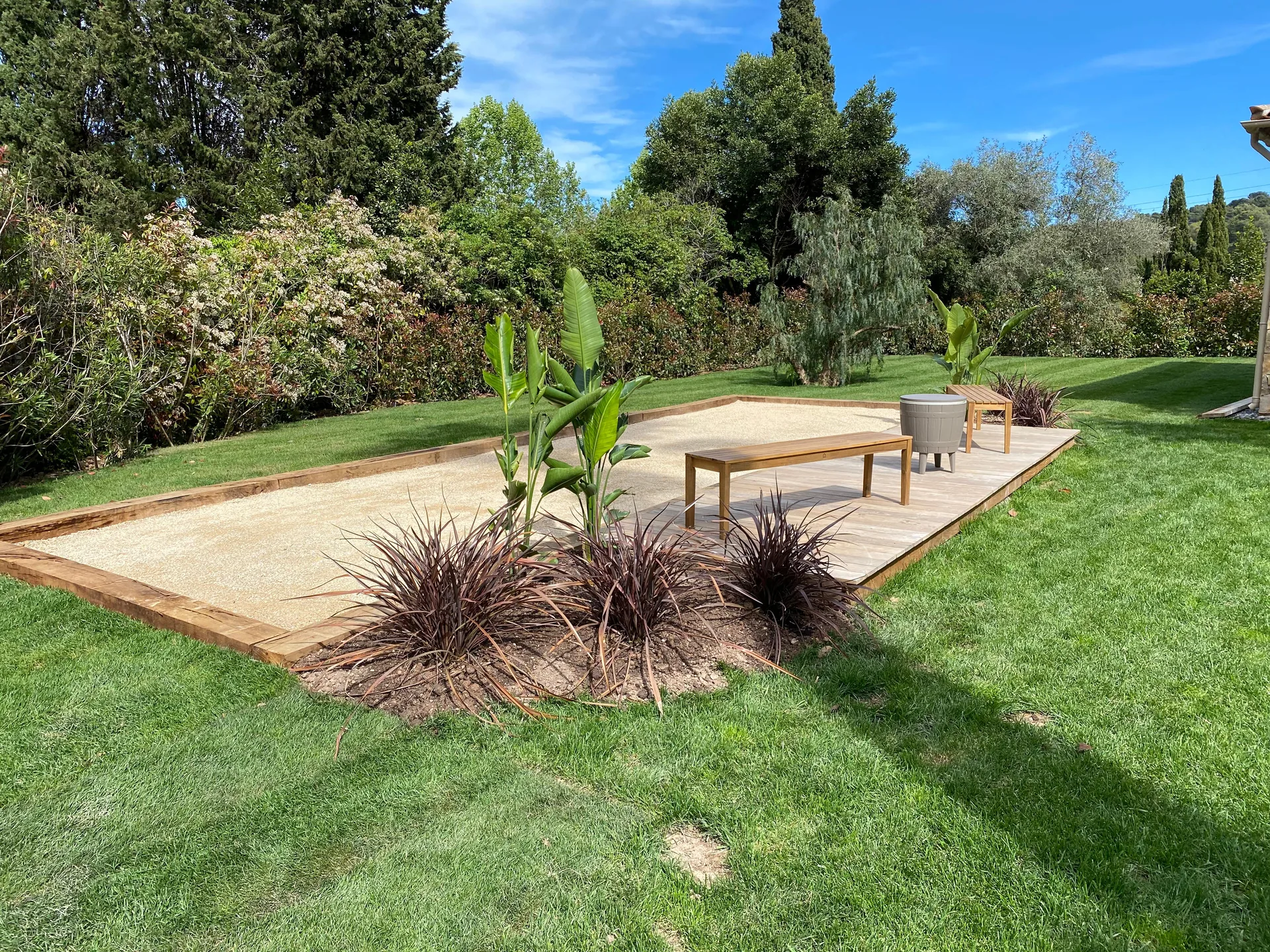Plateforme bois posée sur gazon avec table de jardin et palmiers