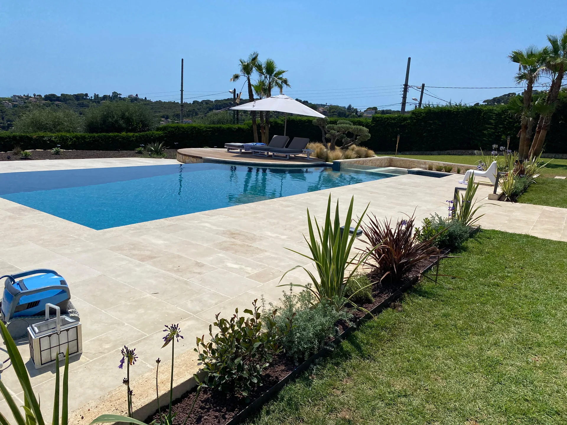 Grande piscine rectangulaire avec parasol et plage en travertin clair